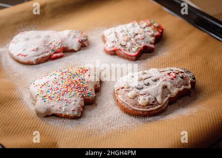 Weihnachtsplätzchen auf einem Backblech mit Puderzucker bestreut. Weihnachtsbaum und Schneemann Cookie Form. Stockfoto