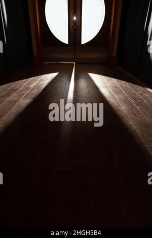 Ein gruseliges Licht von Erie, das durch eine Reihe von Doppeltüren aus Glas auf einen Holzboden mit Korridoreffekt gelangt. Konzeptuelles Bild verschiedene Bedeutungen. Stockfoto