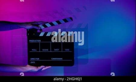 Verschwommene Bilder von Filmschiefer oder Klappbrettwänden. Die Hand hält leere Filmklapeboard auf farbigem Hintergrund im Studio für Filmaufnahmen oder Reco Stockfoto