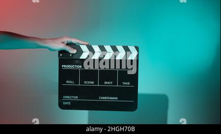 Verschwommene Bilder von Filmschiefer oder Klappbrettwänden. Die Hand hält leere Filmklapeboard auf farbigem Hintergrund im Studio für Filmaufnahmen oder Reco Stockfoto