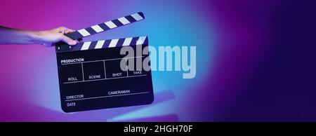 Verschwommene Bilder von Filmschiefer oder Klappbrettwänden. Die Hand hält leere Filmklapeboard auf farbigem Hintergrund im Studio für Filmaufnahmen oder Reco Stockfoto