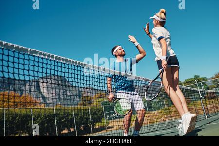 Du machst es unglaublich. In voller Länge geschossen von zwei jungen Tennisspielern, die sich im Freien auf dem Platz gegenseitig eine hohe fünf geben. Stockfoto