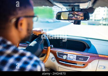 afroamerikanischer Mann, der in einem Auto sitzt und den Rückspiegel nach hinten anpasst Stockfoto