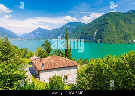 Schöner Blick über den Idrosee Italien. Häuser, ein kleines Dorf auf der Vorder- und blaues Wasser und Berge im Hintergrund. Stockfoto