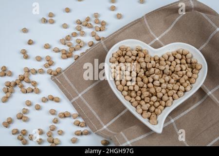 Rohe Kichererbsen auf dem herzförmigen Teller und Handtuch. Draufsicht. Stockfoto