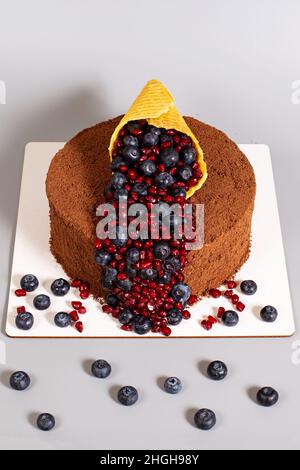 Topping und Schokoladenkuchen aus Waffelkegel und Heidelbeeren mit Granatapfel, Draufsicht auf grauem Hintergrund. Stockfoto