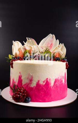 Weiße Sahnehäubchen auf Kuchen mit Beeren und Früchten aus nächster Nähe, auf schwarzem Hintergrund. Stockfoto