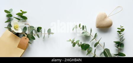 Basteltasche mit Eukalyptus im Winter und weißer Helleborus-Blume. Panorama-Banner. Brauner Papieranhänger, Kopierbereich. Winter flach lag mit immergrünen Zweigen Stockfoto