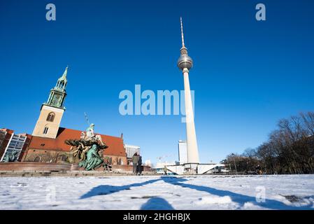 Berlin, Deutschland. 21st Januar 2022. Auf dem Platz vor dem Fernsehturm liegt Schnee unter hellblauem Himmel und Sonnenschein, links der Neptunbrunnen und die St. Mary's Church. Quelle: Christophe Gateau/dpa/Alamy Live News Stockfoto