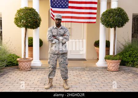 Porträt eines selbstbewussten afroamerikanischen Armeeanmannes in Uniform mit Waffen, die auf der Hausflagge gekreuzt sind Stockfoto