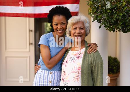 Porträt einer lächelnden afroamerikanischen Tochter mit Arm um die Mutter am Hauseingang Stockfoto