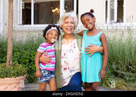 Porträt einer afroamerikanischen Großmutter, die lächelt und ihre Enkelinnen im Freien umarmt Stockfoto