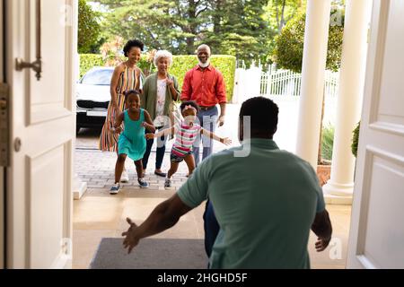 afroamerikanische Mädchen, die zu Hause an der Eingangstür auf ihren Vater zulaufen Stockfoto