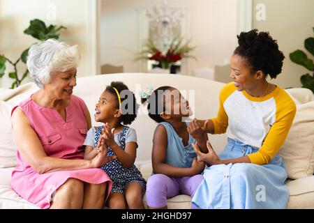 afroamerikanische Großmutter, Mutter und zwei Enkelinnen halten die Hände auf der Couch Stockfoto
