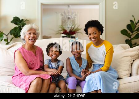 Porträt einer afroamerikanischen Großmutter, Mutter und zwei Enkelinnen, die lächelnd auf der Couch sitzen Stockfoto