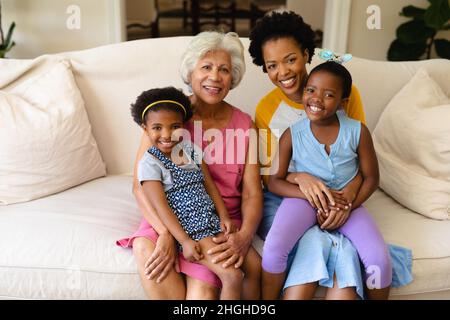 Porträt einer lächelnden afroamerikanischen Großmutter, Mutter und zwei Enkelinnen, die auf der Couch sitzen Stockfoto