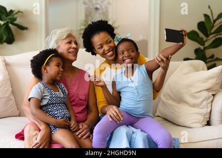 afroamerikanische Großmutter, Mutter und zwei Enkelinnen, die ein Selfie auf der Couch machen Stockfoto