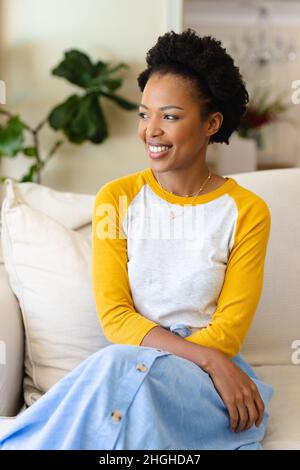 afroamerikanische junge Frau, die lächelnd auf der Couch zu Hause sitzt Stockfoto