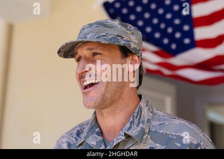 Glücklicher kaukasischer Militärangehöriger mit Mütze und Tarnuniform gegen die us-Flagge Stockfoto