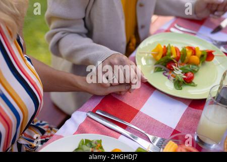 Mittelteil der kaukasischen Mutter und Tochter, die die Hände beim Beten am Esstisch hielten Stockfoto