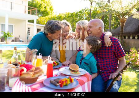 Fröhliche kaukasische Familie aus drei Generationen lacht, während sie im Garten zusammen sitzt Stockfoto