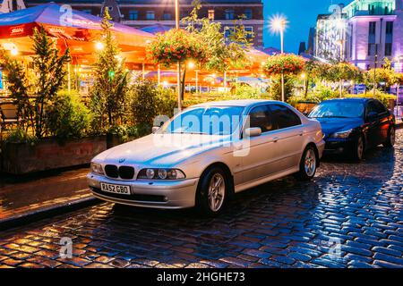 Riga, Lettland. Sedan Car BMW 5 Series E39 Parkplatz in der Nähe von Street Cafe in Abend-oder Nachtbeleuchtung in der Altstadt auf Kalku Street Stockfoto