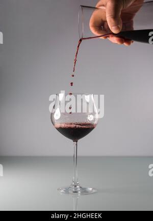 Rotwein, der aus einem Dekanter in ein großes Glas mit neutralem Hintergrund gegossen wird. Stockfoto