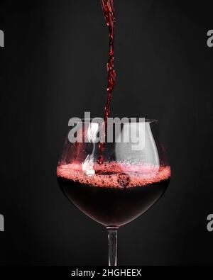 Rotwein wird in einem großen Glas in der Toskana mit neutralem Hintergrund gegossen. Stockfoto