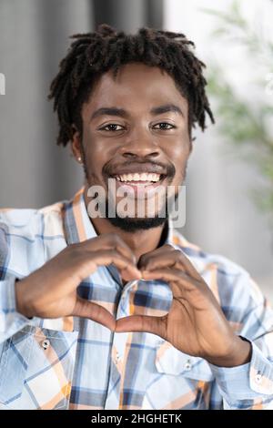 Handsome Guy in Plaid Casual Shirt zeigt Herzgeste an seinen Fingern. Dark Skin Male Model macht Herz Figur durch seine Hände. Verliebte sich. Nahaufnahme. Hochwertige Fotos Stockfoto