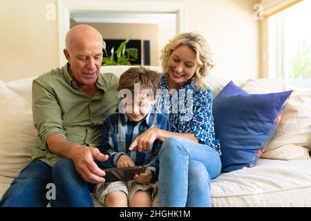 Kaukasische Großeltern und Enkel verwenden ein digitales Tablet, während sie zu Hause auf der Couch sitzen Stockfoto