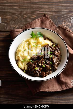 Langsam gegartes Rindfleisch mit Kartoffelpüree in einer Schüssel auf Holzboden. Stockfoto