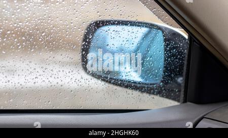 Regen fällt auf eine Seitenscheibe und ein Fenster eines Autos Stockfoto