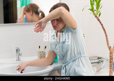 Eine junge Putzfrau in einem hellen Badezimmer mit einem Kolben, um die Verstopfung in ihren Händen zu beseitigen. An der Wand befindet sich ein Spiegel mit Spiegelung. Grüne Pflanze. Stockfoto