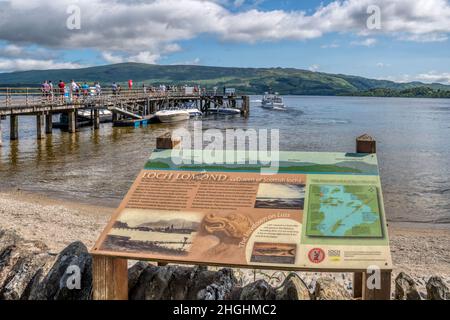 Ein Touristeninformationsschild am Ufer des Loch Lomond am Luss Pier. Stockfoto