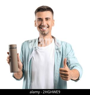 Hübscher junger Mann mit Thermoskanne, der auf weißem Hintergrund Daumen hoch zeigt Stockfoto