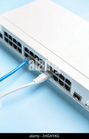 Moderner Kommutator mit Internetkabeln auf blauem Hintergrund, Nahaufnahme Stockfoto