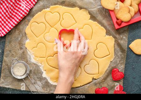 Frau bereitet herzförmige Kekse am Tisch zu. Valentinstag-Feier Stockfoto