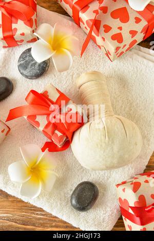Spa-Steine, Geschenkboxen, Kräuterbeutel und Handtuch auf dem Tisch. Valentinstag-Feier Stockfoto