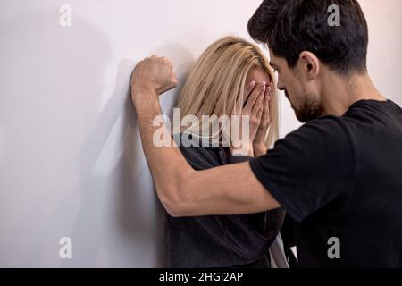 Männer attackieren Frau, häusliche Gewalt. Betrunkener Ehemann schlägt Ehefrau. Ein aggressiver Mann trifft weinend die junge Frau, weiblich. An die Wand geklemmt und verängstigt. Fam Stockfoto