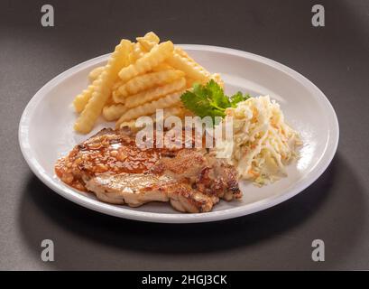 Traditionelle Chicken-Chop-Sauce mit pommes Frites auf weißem Teller, Draufsicht auf dunkelgrauem Hintergrund Stockfoto