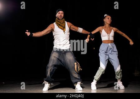 Aktive Männer und Frauen tanzen Hip-Hop in legerer Kleidung auf schwarzem Hintergrund in der Tanzhalle mit weißem Licht. Jugendkultur, Hip-Hop, Bewegung, Stil und Stockfoto