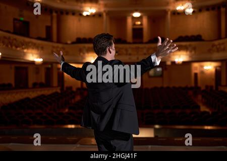 Showman. Männlicher Entertainer, Moderator oder Schauspieler im mittleren Alter auf der Bühne. Arme an den Seiten. Ansicht von hinten Porträt eines hübschen kaukasischen männlichen öffentlichen Sprechers in Stockfoto