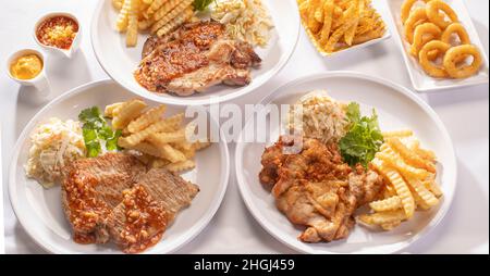 Gemischtes Grillrestaurant mit vollem Tisch Sirloin-Steak, Schweinekotelett, gegrillter Lammkotelett, Hühnerschnitzel, Käsefritzen Nieselregen, Zwiebelringe, französisch f Stockfoto