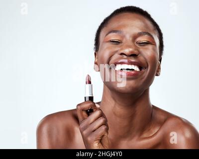 Lippenstift für einen natürlichen Look. Studioaufnahme einer schönen jungen Frau, die roten Lippenstift auf einem grauen Hintergrund auflegt. Stockfoto