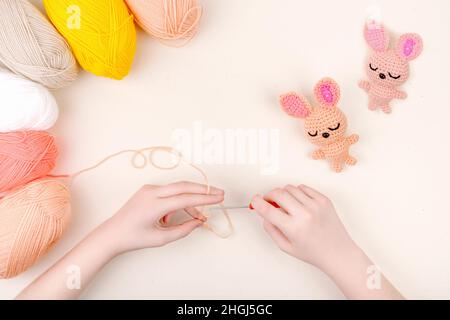 Kinderhände häkeln einen Spielzeughasen. Kreativität, Handwerk, handgemachtes Konzept. Stockfoto