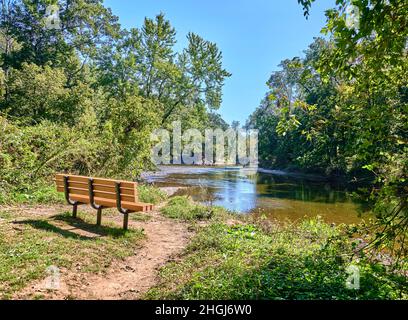 Leere Parkbank mit Blick auf einen See, Teich namens Neshaminy Creek im Tyler State Park in Bucks County, Pennsylvania USA. Stockfoto