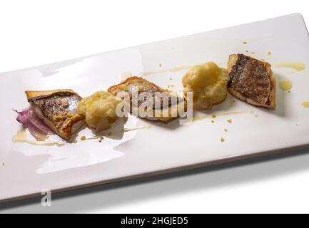 Gebratenes Seebarschfilet mit Blumenkohl, Zwiebeln und geriebener Zitronenschale auf einem weißen rechteckigen Teller Stockfoto