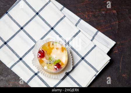 Kuchen mit Gelee, Kiwi, Kirschen und Mango auf dem Tisch. Leckeres Mini-Dessert auf einem hölzernen Hintergrund, Nahaufnahme. Stockfoto