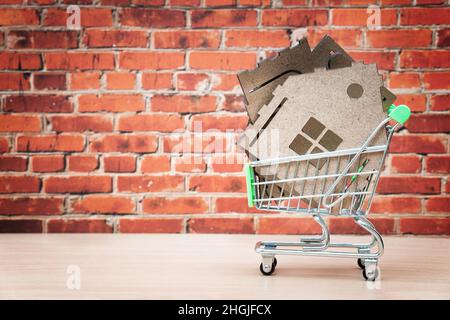 Teile eines Miniatur-Haus-Modellbausatzes in einem kleinen Warenkorb vor einem roten Backsteinwand-Hintergrund. Home Verbesserung und Reparatur-Konzept. Stockfoto