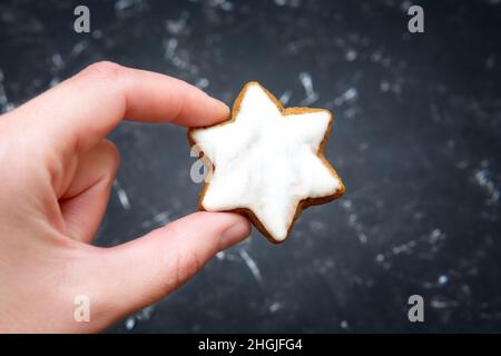 Sternförmiger Zimtkeks in der Hand auf schwarzem Hintergrund. Traditionelles Weihnachtsbacken. Stockfoto